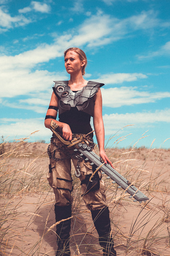 Futuristic Female Warrior Standing In The Desert. She is by herself and carries a weapon.