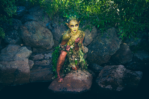 Pretty Water Nymph Fantasy Creature Near a Creek. Young woman wearing stage makeup and acting outdoors.