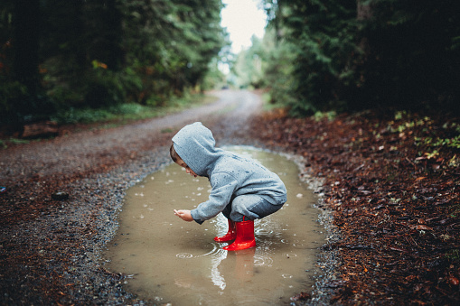 A cute group of kids wearing rain boots splash and play in a big mud puddle, enjoying the discovery and excitement of being outdoors and experiencing nature.