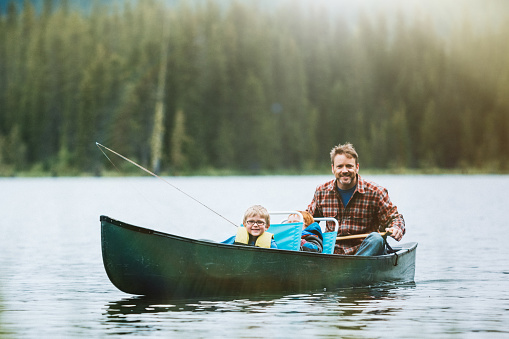 A dad and his boys enjoy some time at the lake, fly fishing for trout from the shore and a canoe.  A depiction of a involved and supportive father. Shot at Trillium Lake in Oregon state.