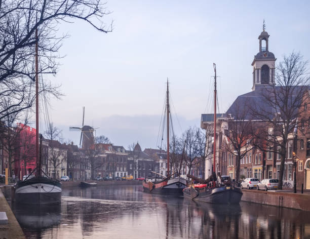 Old Dutch city Schiedam morning landscape during winter calm weather with reflections in a freezing canal, old barges and windmill stock photo