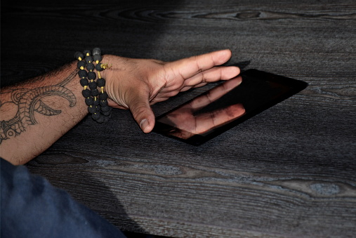 A close-up of a Polynesian arm with Ta Moko (Polynesian Tribal Tattoo) holding a Digital Tablet.