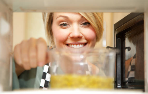 female cook heating food in microwave stock photo