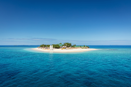 Beautiful small island in the middle of the south pacific ocean with beach huts, lounge chairs, palm trees, surrounded with beautiful clear turquoise water. Islet, Mamanuca Islands, Fiji, Melanesia