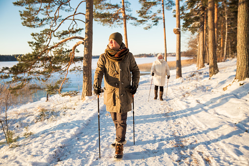 Winter sport in Finland - nordic walking. Man and Senior woman hiking in cold forest. Active people outdoors. Scenic peaceful Finnish landscape with snow.