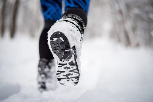 Shoe sole of a person walking on the path covered with snow.