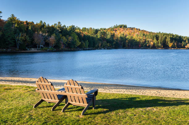 leere adirondack stühle mit blick auf einen see bei sonnenuntergang - adirondack chair stock-fotos und bilder