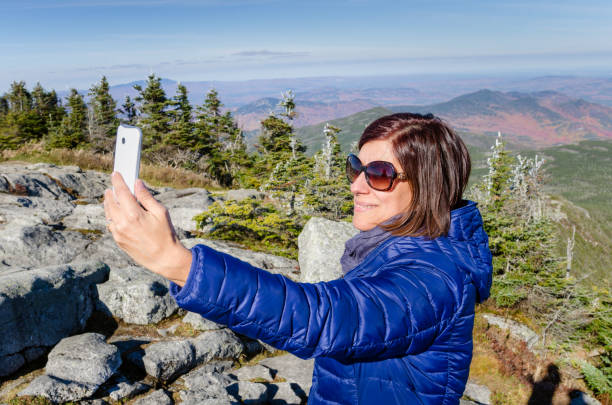 Woman Taking a Selfie with a Smartphone on the Summit of a Mountain Young Woman Tourist Taking a Selfie with a Smartphone on the Peak of a Mountain on a Sunny Autumn Day. Whiteface Mountain, Adirondacks, NY whiteface mountain stock pictures, royalty-free photos & images