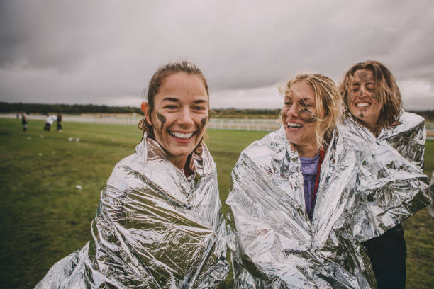 We Won! Women are wrapped up in foil blankets after completing a charity obstacle course. One of the women is looking at the camera and they are all covered in mud. mud photos stock pictures, royalty-free photos & images