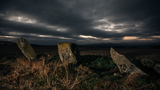 A row of prehistoric standing stones in a field near Stirling, Scotland, at sunset. Erected around four thousand years ago and carved with cup-mark decorations in the top surface, the purpose of both the monument and the rock art are unknown.