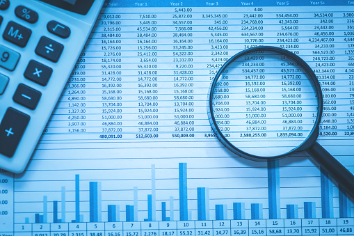 Spreadsheet bank accounts accounting with calculator and magnifying glass. Concept for financial fraud investigation, audit and analysis.