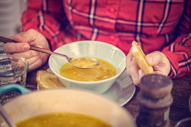 Little girl eating delicious chicken soup with carrots, onions and parsnips. The soup is served in a bowl with creme fresh and grilled toast.