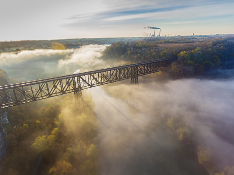 Sun rises over old railroad bridge and river while hydroelectric plant is visible in the background