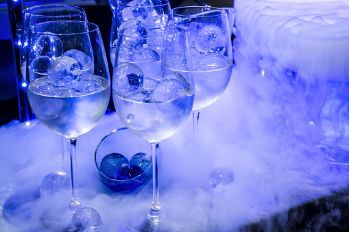 Glasses with cocktails and ice on a bar in a night club. Colorful spot lights, UV lights and smoke create an attractive ambience.
