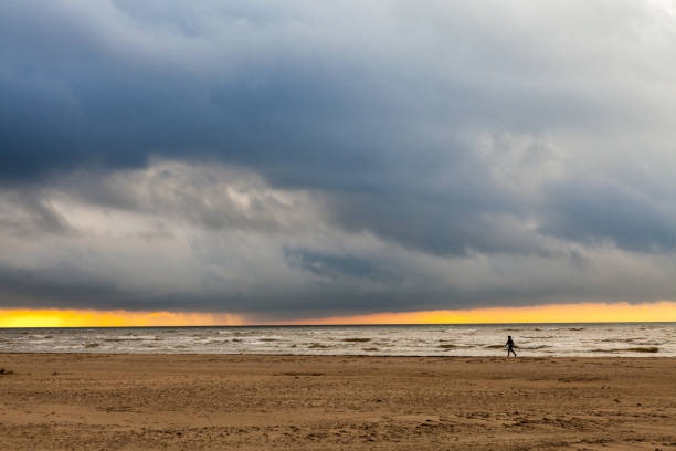 Man walking along the sea shore at sunset stock photo