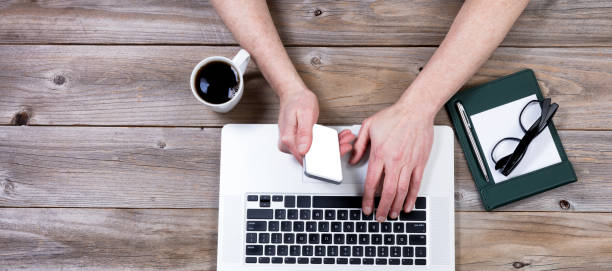 istock Top view of working desktop with hand holding smartphone 640963304