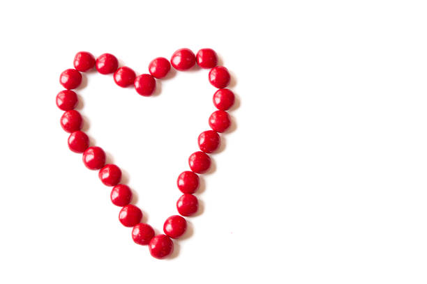 Red cinnamon candy jelly beans creating a heart shape with an arrow on white background