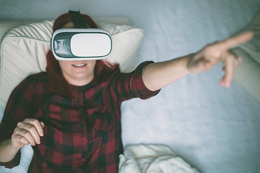 Woman in virtual reality helmet on bed. VR glasses.