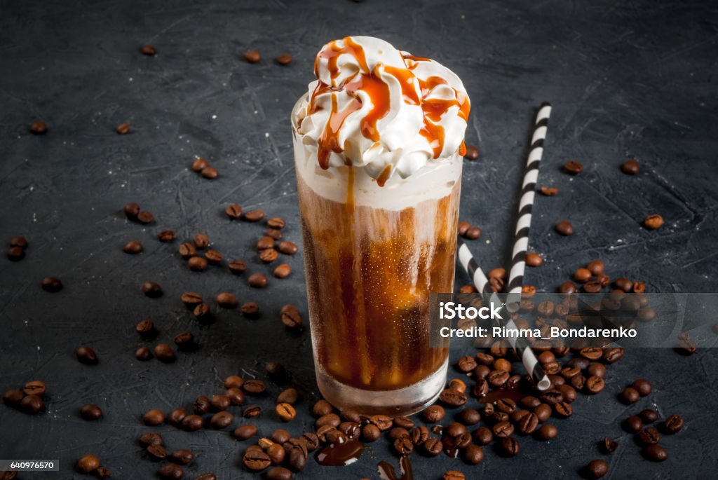 Cold coffee drink frappe Cold coffee drink frappe with whipped cream and caramel syrup, with straws and grains of coffee on a dark gray stone table, copy space Cappuccino Stock Photo