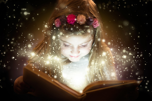 Beautiful little girl smiling and reading her magic book