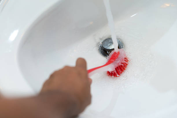 Woman cleaning washbasin with a brush and running water.