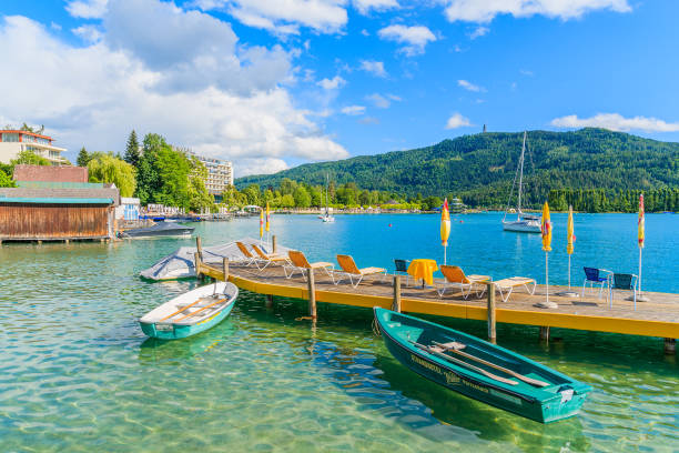 WORTHERSEE LAKE, AUSTRIA WORTHERSEE LAKE, AUSTRIA - JUN 20, 2015: tourist boats and sunchairs with umbrellas on wooden pier of beautiful alpine lake Wort pörtschach am wörthersee stock pictures, royalty-free photos & images
