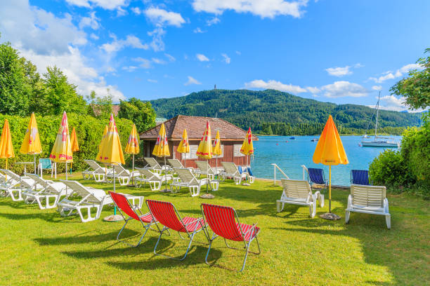 WORTHERSEE LAKE, AUSTRIA WORTHERSEE LAKE, AUSTRIA - JUN 20, 2015: sunchairs with umbrellas on beach of beautiful alpine lake Worthersee in summer. pörtschach am wörthersee stock pictures, royalty-free photos & images