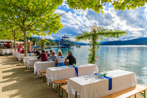 WORTHERSEE LAKE, AUSTRIA - JUN 20, 2015: people sitting at tables along Worthersee lake shore during summer beer festival.