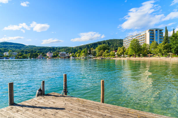 WORTHERSEE LAKE, AUSTRIA WORTHERSEE LAKE, AUSTRIA - JUN 20, 2015: wooden pier and hotel building along Worthersee lake shore in summer season. pörtschach am wörthersee stock pictures, royalty-free photos & images