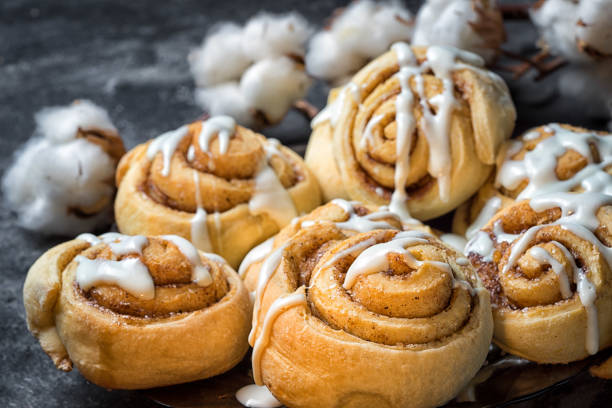 chiudere i rotoli di cannella in un piatto, su uno sfondo scuro con scatole di cotone di cemento dietro. - cake dessert pastry pastry crust foto e immagini stock