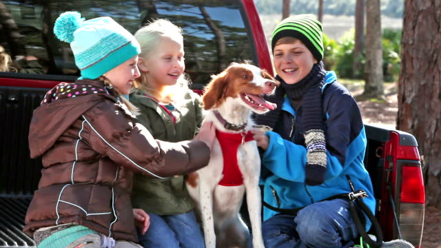 Three children petting their dog, a brittany spaniel