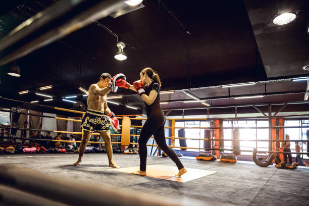 Muay Thai workout - Motivational training at the gym facility Modern gym facility in Bangkok, young athletes training for a Muay Thai class, women and men boxing gym stock pictures, royalty-free photos & images