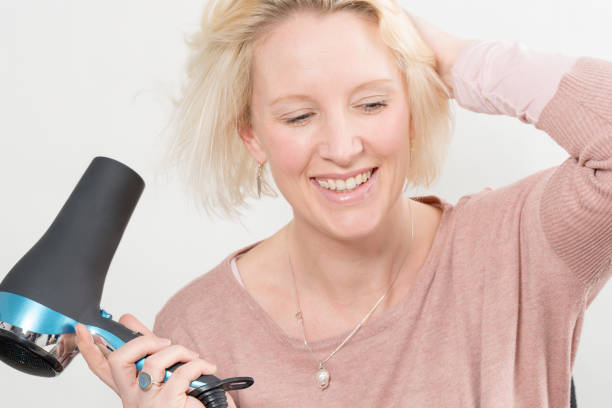 Blonde Woman Smiling While Drying Her Hair Using Blow Dryer