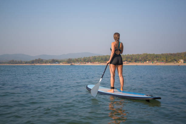 A girl standing on a StandUp Paddle board close to a beach in Goa, India.