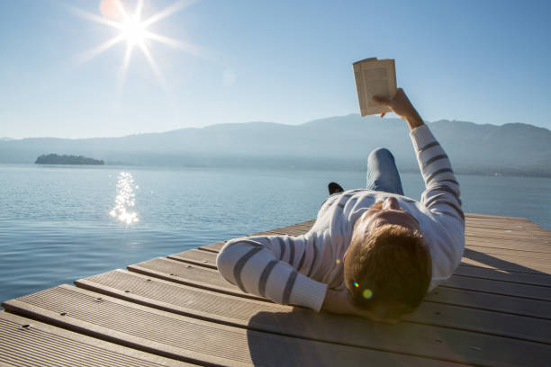 istock Young man relaxing on lake pier, reads book 641036132