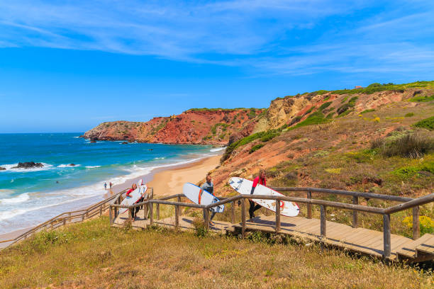 praia do amado beach, portugal - 15 de maio de 2015: surfistas andando na passarela da bela praia na região do algarve. surf é um esporte popular em portugal ocidental sul devido a frequentes ventos fortes. - surf sand rock coastline - fotografias e filmes do acervo