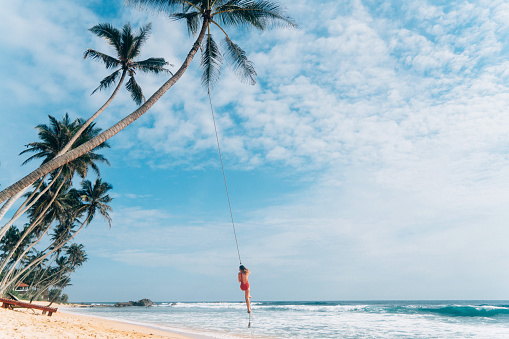 Young Caucasian woman playing on the rope swing on the beach in Sri Lanka