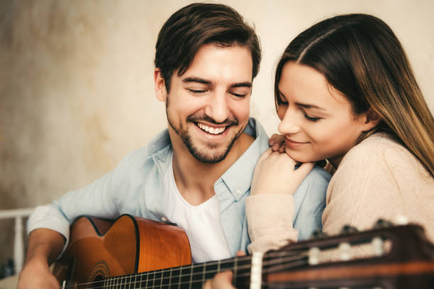 young couple playing acoustic guitar young couple playing acoustic guitar kiss entertainment group stock pictures, royalty-free photos & images