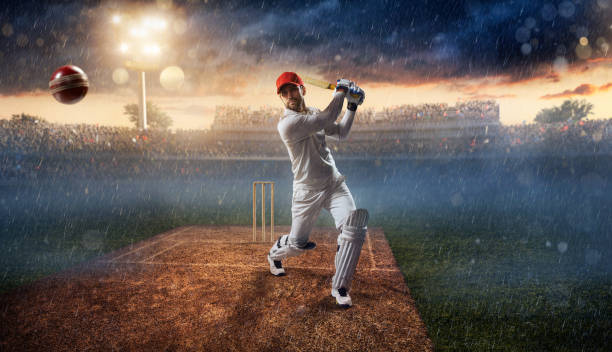 Cricket: Batsman on the stadium in action Cricket batsman bouncing a ball. He is wearing unbranded sports cloth and equipment. The bleachers full of people are blurred behind the player. There is a rain falling from the dark skies and intentional lenseflares on the image. The stadium is made in 3D. batsman photos stock pictures, royalty-free photos & images
