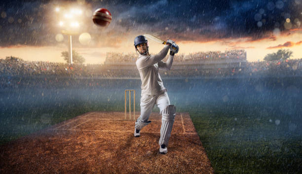 Cricket: Batsman on the stadium in action Cricket batsman bouncing a ball. He is wearing unbranded sports cloth and equipment. The bleachers full of people are blurred behind the player. There is a rain falling from the dark skies and intentional lenseflares on the image. The stadium is made in 3D. cricket player photos stock pictures, royalty-free photos & images