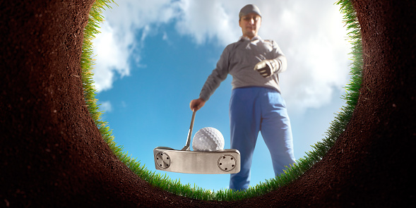 Man playing Golf on Golf course. Point of view from inside the hole. The course is made in 3D. The man wears unbranded cloth and hold unbranded equipment.