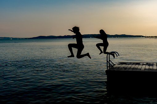 Shiluette of boy and girl jumping in the lake from pier