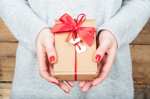 Hands holding gift in kraft box on a wooden background. The concept of St. Valentine's day, weddings, engagements, Mother's Day, birthday, New Year, Christmas, holidays.