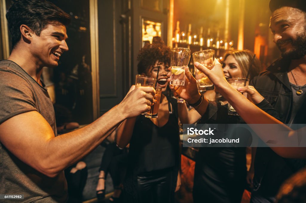 Group of men and women enjoying drinks at nightclub Group of men and women enjoying drinks at nightclub. Young people at bar toasting cocktails and laughing. Happy Hour Stock Photo