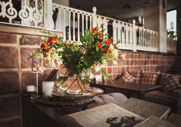 Still life with a cup of coffee on the wooden saucer and coffee bean in burlap sack and fresh flower bouquet in a glass which has black background.