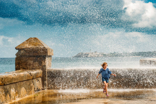 Cuba with Children Little girl running away from the waves crashing on Havana's Malecón. Cuba. morro castle havana stock pictures, royalty-free photos & images