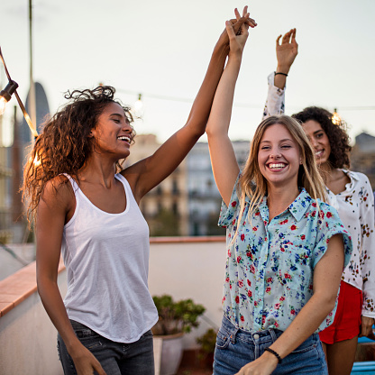 Cheerful women dancing with arms raised during party. Happy female friends are enjoying on terrace. Multi-ethnic people are celebrating during sunset.