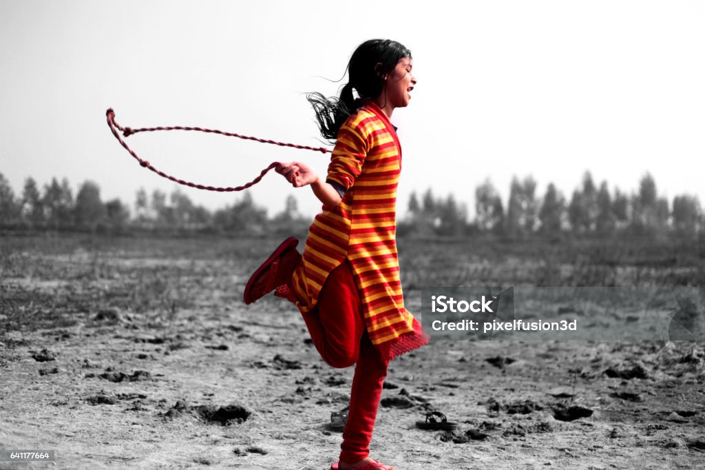 Rope Jumping Game Village girl playing with jumping rope in playground. Child Stock Photo