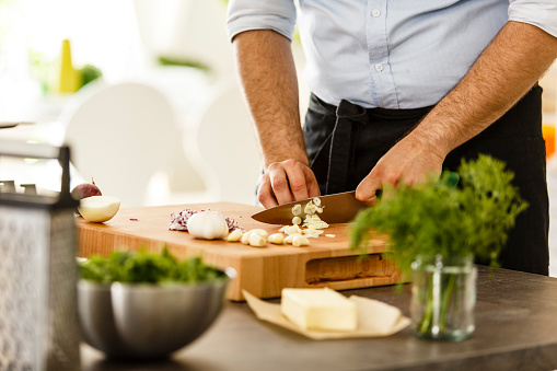 Chef slicing garlic on cutting board in the kitchen, preparing meal.