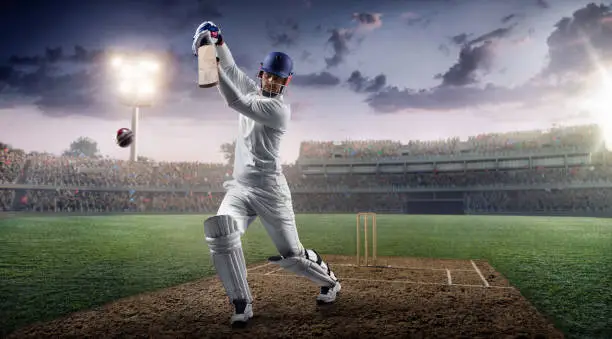 Cricket bouncing a ball on a cricket field. The batsman is wearing unbranded sports cloth and equipment. The bleachers full of people are blurred behind the player. Background is made in 3D. There are intentional lenseflares on the image.